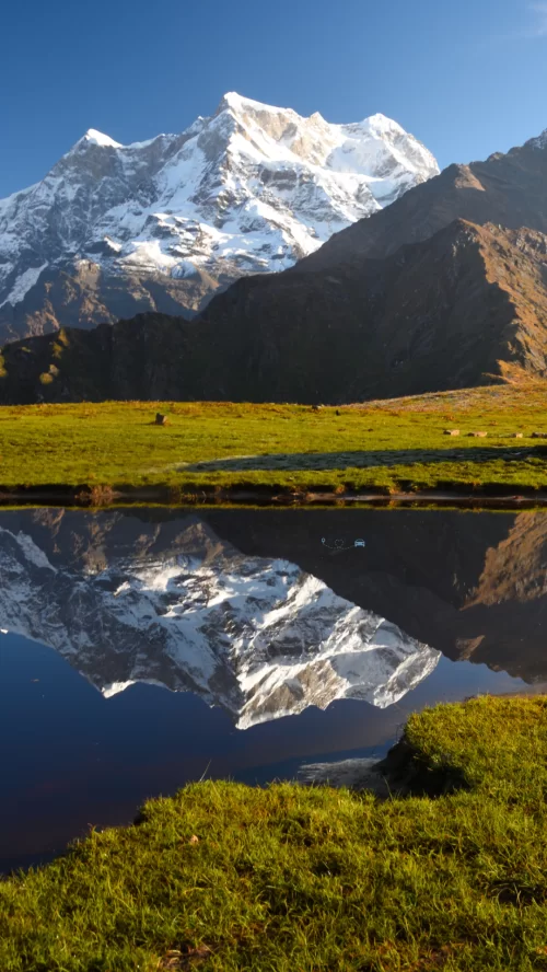 Majestic snow-clad Chaukhamba Peak reflecting in a serene lake near Madhyamaheshwar Temple, Uttarakhand—a divine trek destination in Uttarakhand tour packages.