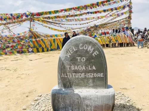 Tsaga La Pass Ladakh welcome stone monument altitude 5200m multicolored Tibetan prayer flags tourists motorcycles gravel ground blue sky; high-altitude adventure Leh photography heritage package.