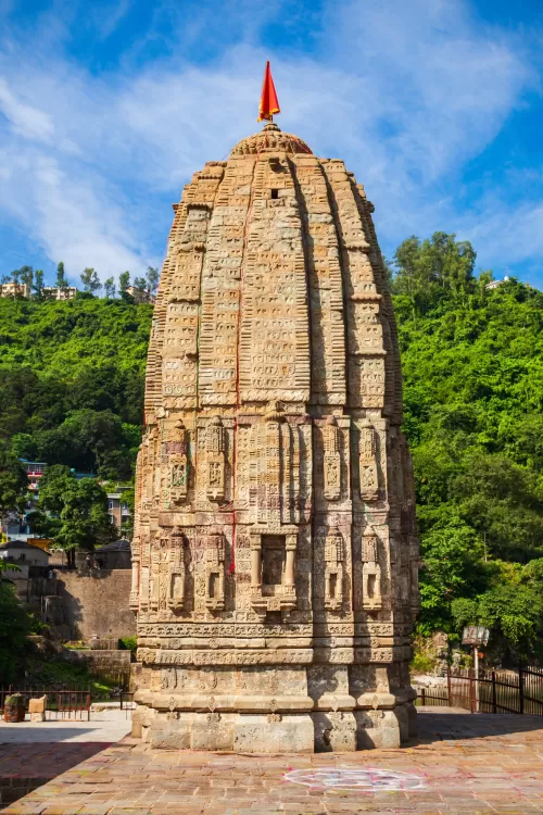Ancient stone temple with intricate carvings in Mandi surrounded by lush hills, a historic landmark featured in Himachal Pradesh tour packages.