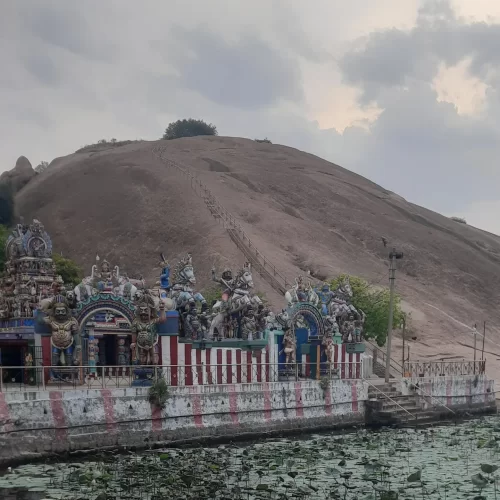 Samanar Hill Tamil Nadu Samanamalai Jain temple base colorful gopuram towers deities horses steps brown rocky hill lotus pond cloudy sky lamp post railing, ancient Jain temple hill temple tour package. 