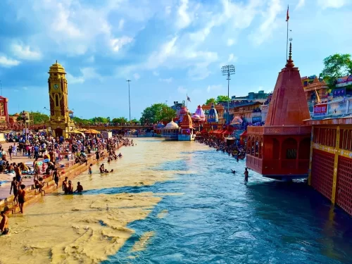 Har Ki Pauri Haridwar vibrant Ganga ghats with golden clock tower temples devotees bathing colorful umbrellas blue sky clouds, perfect spiritual bathing ghat, Uttarakhand tour packages.