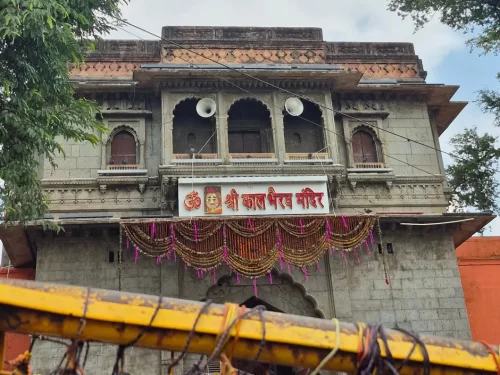 Shree Kaal Bhairav Temple gate at Ujjain during clear daylight, featuring grey stone arch red signboard garlands devotees, perfect spiritual Madhya Pradesh tour package.