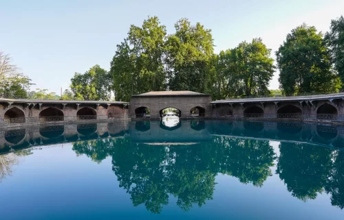Octagonal Verinag spring pavilion during blue sky, featuring clear pool reflections & chinar trees, perfect romantic experience Kashmir tour packages.